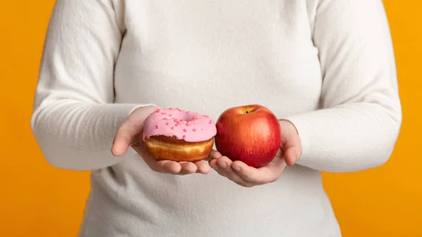 Felismerhetetlen elhízott nő fánkot és almát tart a kezében. — Stock Fotó