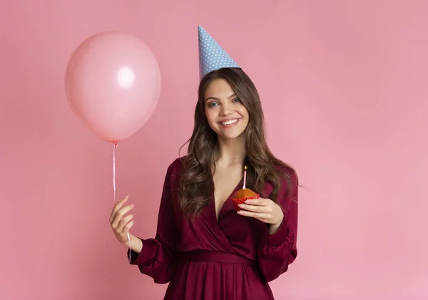 Happy young girl holding balloon and cupcake with lighted candle — Stok fotoğraf