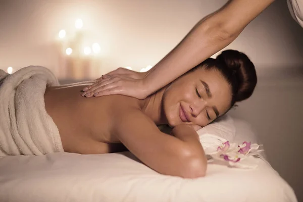 Mulher recebendo massagem clássica nas costas com velas no fundo — Fotografia de Stock