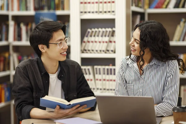 Két mosolygó multikulturális diák tanul a könyvtárban. — Stock Fotó