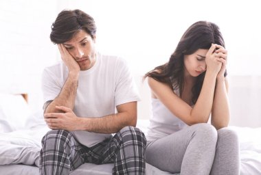 Desperate man and woman sitting on bed after hard talk