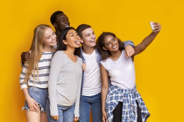Cheerful group of multiethnic friends taking selfie over yellow background