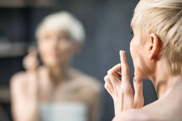 Mujer irreconocible de mediana edad que aplica crema facial anti-envejecimiento en el baño —  Fotos de Stock