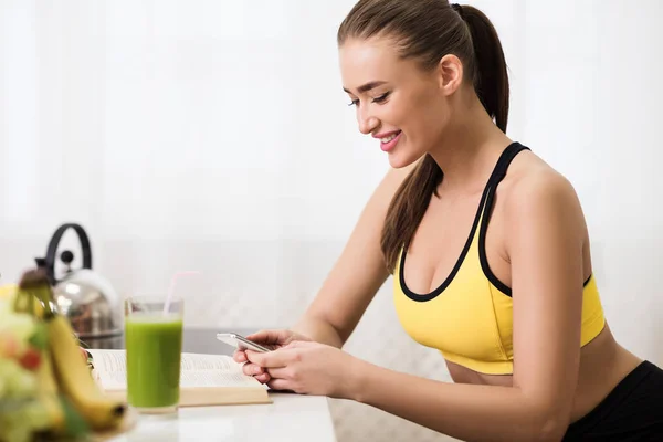 Sporty girl texting on cellphone and drinking detox smoothie — Stockfoto