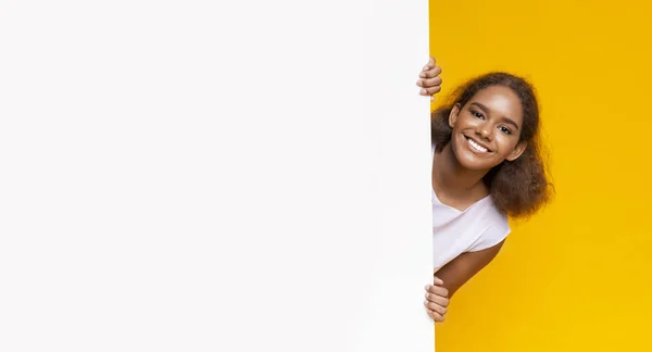 Menina afro alegre olhando de grande placa branca para publicidade — Fotografia de Stock