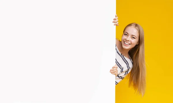 Excited girl looking from behind blank advertising board — Stok fotoğraf