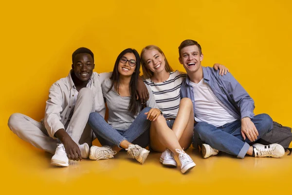 Happy students posing over yellow studio background