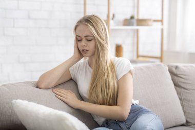 Blonde girl sitting on sofa, suffering from migrane