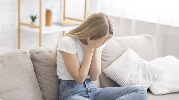 Відчайдушна молода жінка плаче на дивані вдома — стокове фото