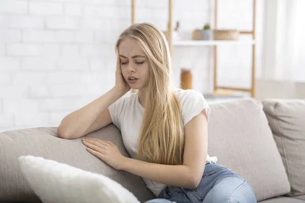 Blonde girl sitting on sofa, suffering from migrane — Stockfoto