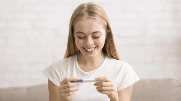 Щаслива молода жінка дивиться на тест на вагітність в руках — стокове фото