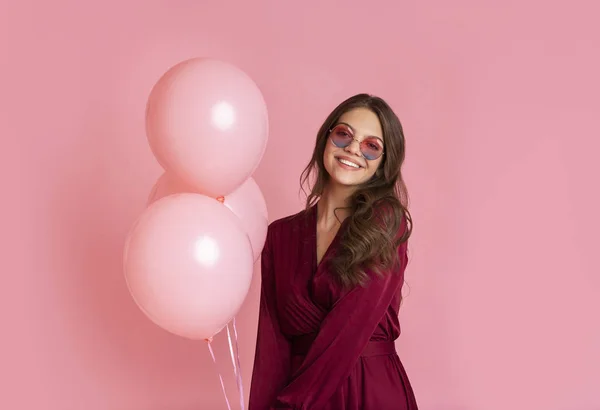 Pretty Girl en gafas de sol con estilo posando con globos sobre fondo rosa — Foto de Stock