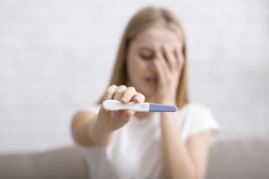 Üzgün genç bir kadın tarafından yapılan pozitif hamilelik testi.