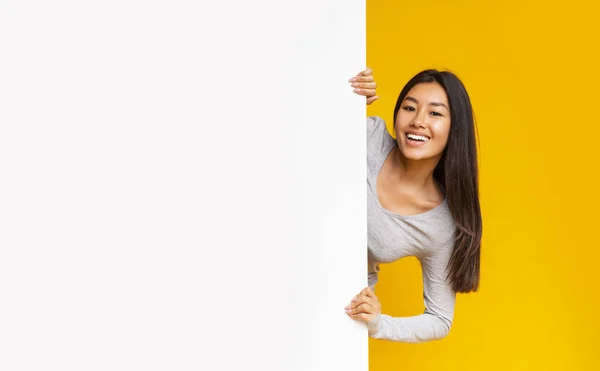 Menina asiática bonita olhando de trás placa de publicidade branca — Fotografia de Stock