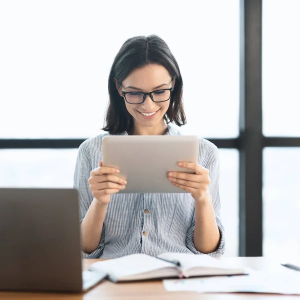 Ung flicka som håller tablett och använda laptop på kontoret — Stockfoto