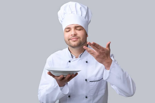 Chlápek šéfkuchař drží talíř čichání nádobí přes šedé pozadí — Stock fotografie