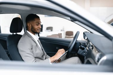 Araba satıcısı, galeride otomobilde oturan notlar alıyor.