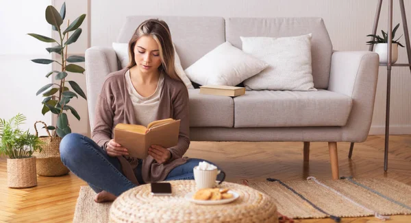 Giovane donna che legge libro, seduta sul pavimento a casa — Foto Stock