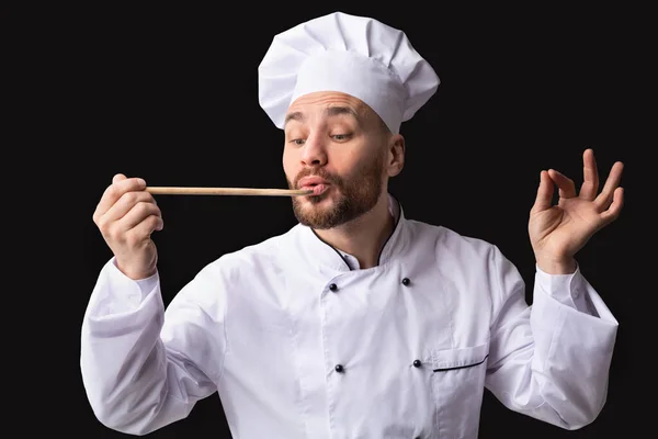 Cozinheiro homem degustação prato sobre fundo preto estúdio — Fotografia de Stock