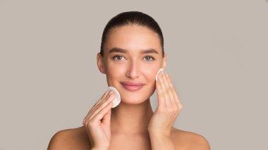 Yüz bakımı. Gri arkaplan üzerinde pamuk pedi kullanan kız