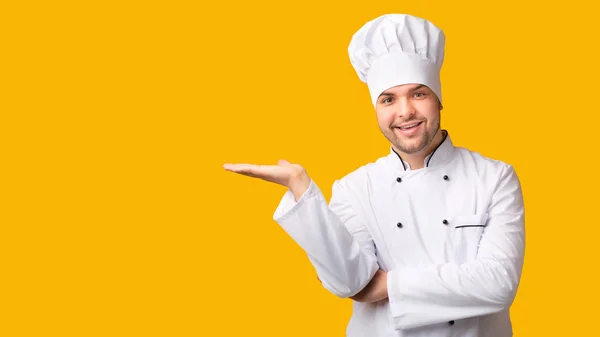 Szef kuchni trzyma niewidzialny obiekt na otwartej dłoni, żółte tło — Zdjęcie stockowe
