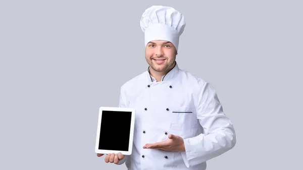 Kuchař drží tablet zobrazující prázdný displej, šedé pozadí, Mockup — Stock fotografie