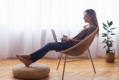 Genç bir kadın dizüstü bilgisayarda geziniyor, kahveyle rahatlıyor.