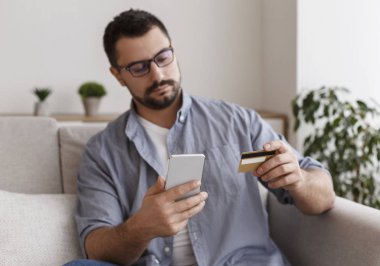 Concentrated young man doing shopping online with smartphone