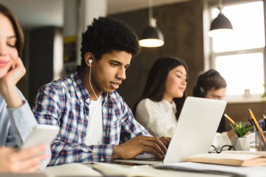 Üniversite kütüphanesinde laptopla çalışan zeki bir afro çocuk.