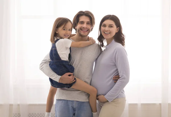 Cheerful pregnant mother, father and their daughter posing together at home — Stok fotoğraf