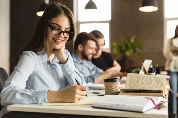 Estudiante confiado. Chica feliz sentada en la biblioteca y tomando notas — Foto de Stock