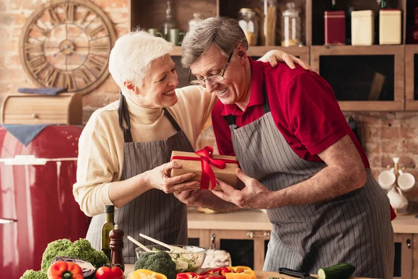 Loving senior woman giving gift box to her husband at kitchen — Φωτογραφία Αρχείου
