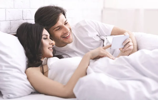 Fiatal házaspár néz fényképeket mobiloddal — Stock Fotó