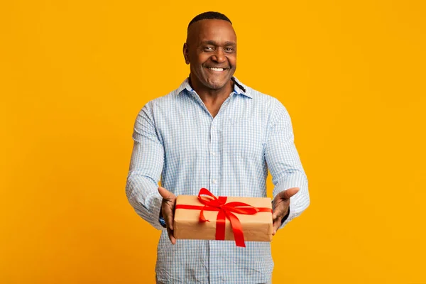 Gelukkig volwassen afrikaanse amerikaanse man geven gift box op camera — Stockfoto