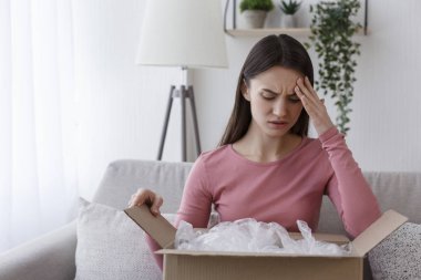 Üzgün kadın müşteri karton paketi boşaltıyor.