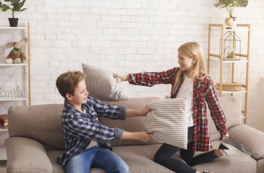 Sibling Having Fun Fighting With Pillows On Couch Indoor
