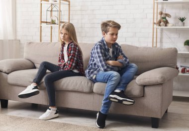 Offended Brother And Sister Sitting Back-To-Back On Sofa At Home