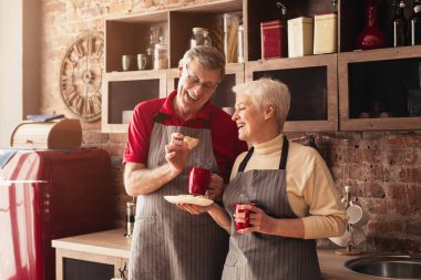 Portrait Of Senior Couple Drinking Coffee And Eating Cookies In Kitchen