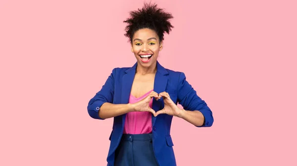 Mosolygós afro lány bemutató szív gesztus rózsaszín stúdió — Stock Fotó