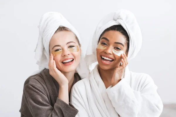 Joyful young women in bathrobes applying eye patches — Stock Fotó