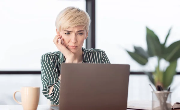 Sério mulher de negócios no laptop sentado tocando queixo no escritório — Fotografia de Stock