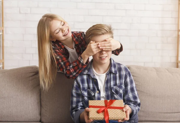 Дівчина покриває братами очі даруючи йому подарунок день народження в приміщенні — стокове фото