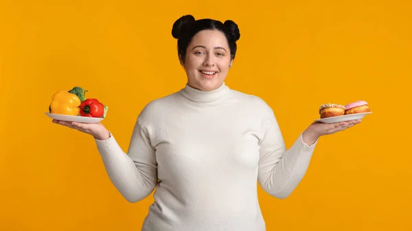 Smiling Plus Sized Girl Holding Plates With Fresh Vegetables And Donuts — ストック写真