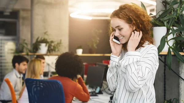 Emotional redhead girl having conversation on phone in office