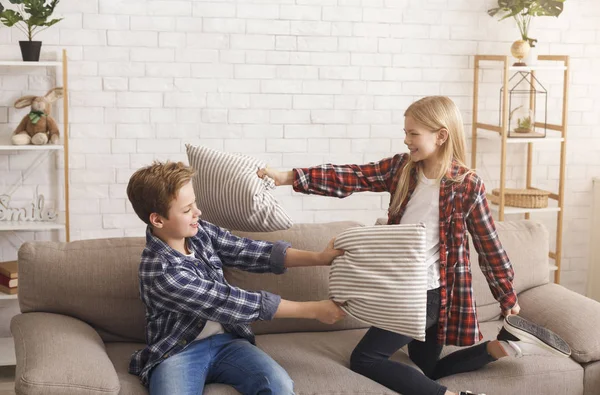 Sibling Having Fun Fighting With Pillows On Couch Indoor — стокове фото