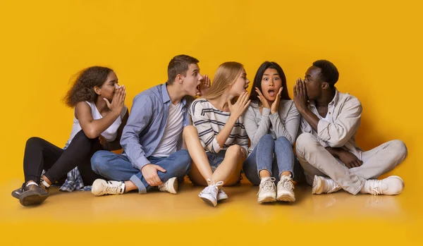 Grupo de amigos multirraciais fofocando sobre fundo amarelo — Fotografia de Stock