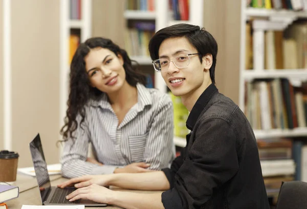 Sorridente casal multicultural aprendendo na biblioteca moderna — Fotografia de Stock