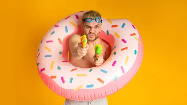 Young guy having fun with water guns, swim goggles and inflatable ring — Stock Fotó