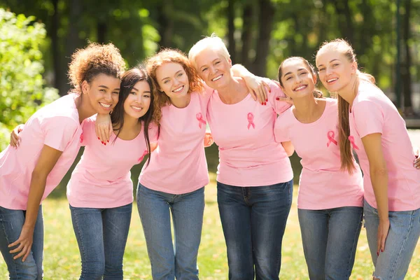Mutiracial señoras en rosa camisetas con cintas abrazando de pie al aire libre — Foto de Stock