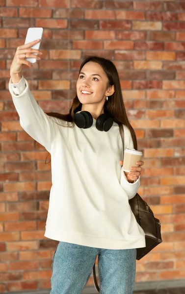 Beautiful young girl smiling, doing selfie, holding coffee — Zdjęcie stockowe